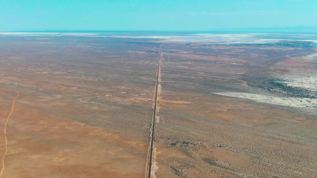Aerial view of a straight line crossing flat desert plains under blue sky.