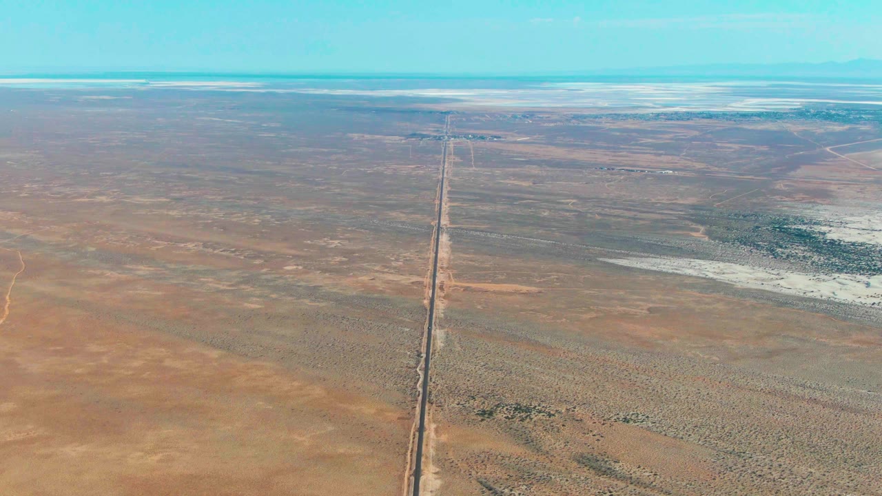 Second aerial frame in Guerrero Negro, Baja California Sur, showing the straight corridor slightly right of center across dry plains with pale salt-like ground patches and no visible people.