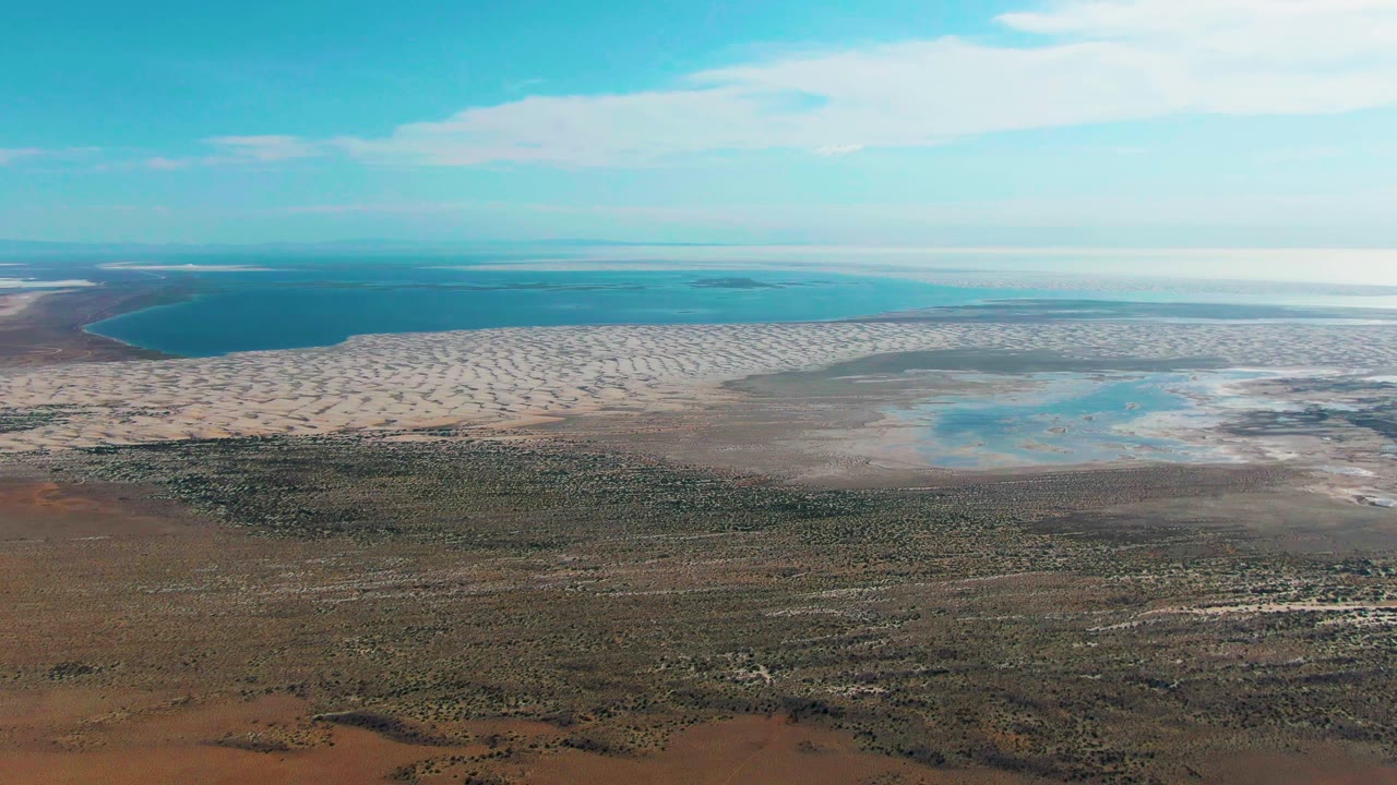Coastal aerial with shallow water pools beside sandy flats and open land.