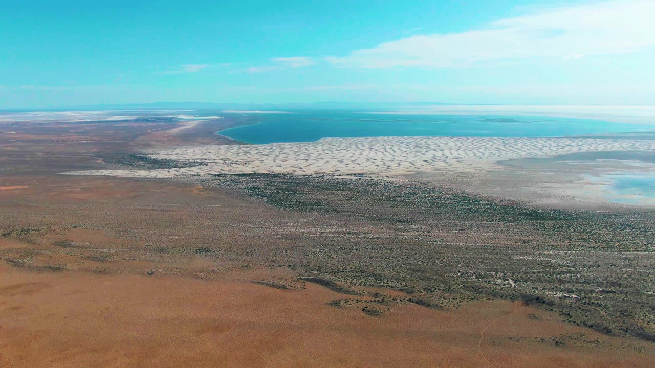 Wide aerial coastline with brown desert foreground and pale tidal shoreline.