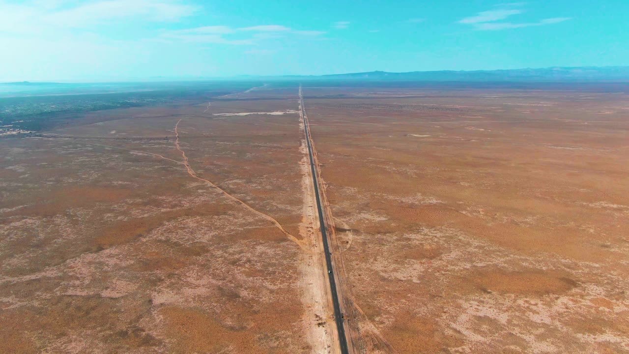 Aerial view of a straight desert road running toward distant mountains.