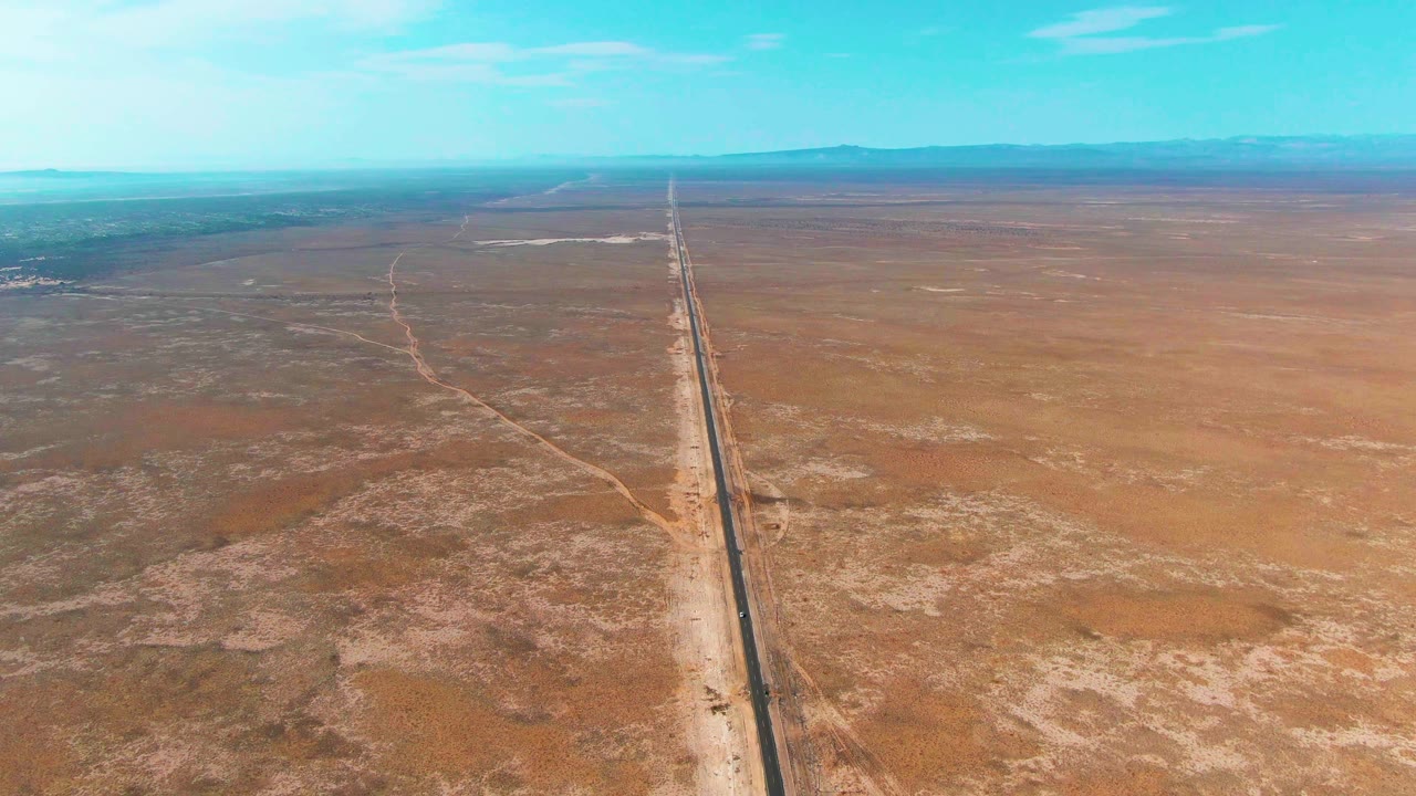 Aerial view in Guerrero Negro, Baja California Sur, with the straight road more centered through scrubby desert and a low mountain horizon, with no visible people.