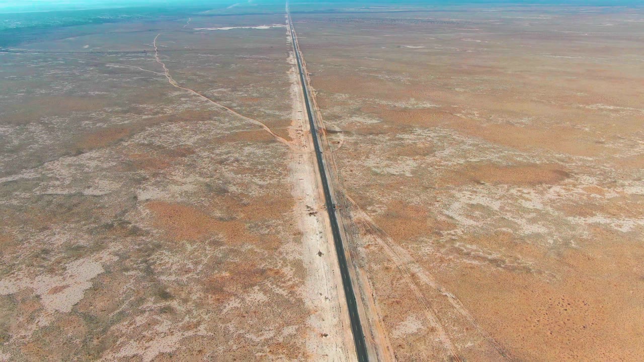 Aerial view of a straight road crossing brown desert terrain.