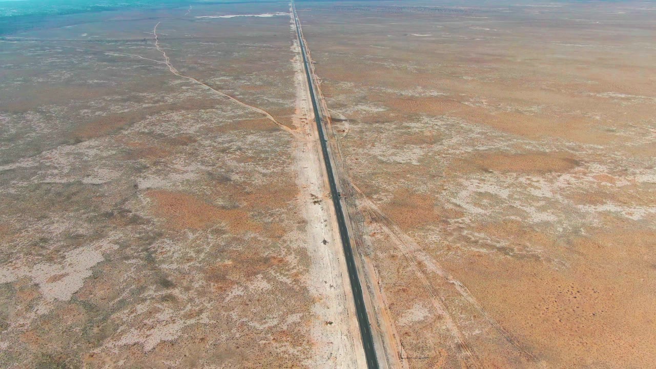 Aerial view in Guerrero Negro, Baja California Sur, with the paved road set slightly right of center, pale road shoulders, patchy desert textures, and no visible people.