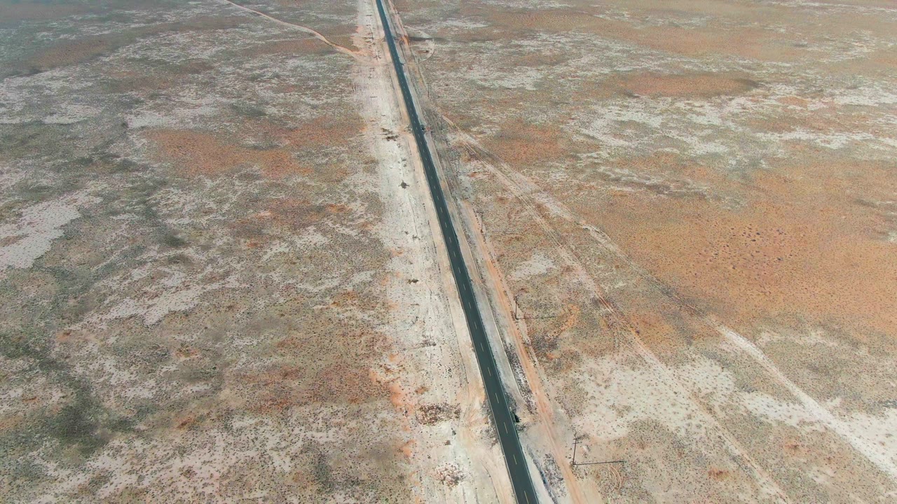 The 0:02 frame shows a straight Guerrero Negro highway bordered by pale road shoulders, sandy desert flats, scattered scrub, and no visible people.