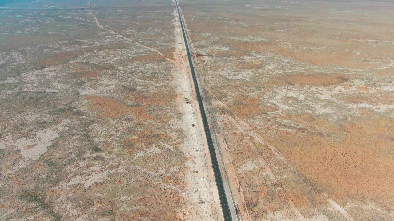 Aerial view of a straight road crossing dry desert terrain.