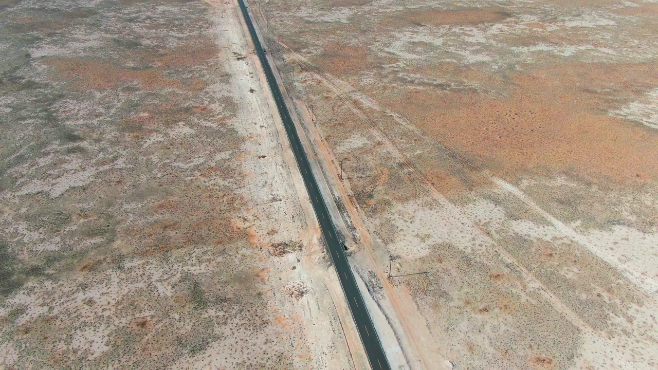 Small vehicle on a straight desert highway viewed from above.