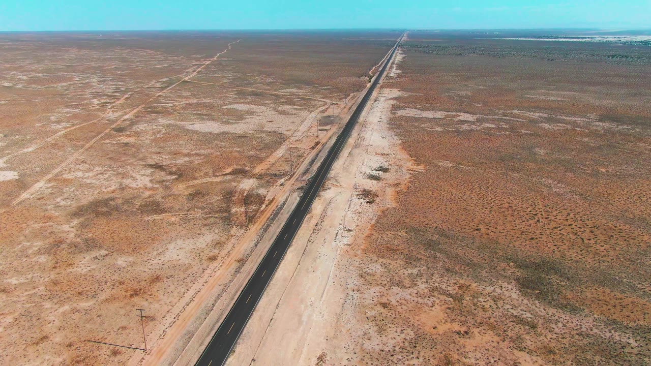 Aerial view of a straight desert road crossing sandy terrain.