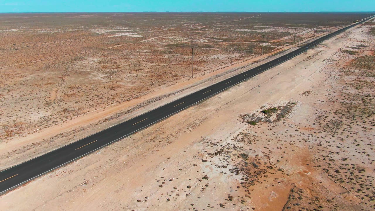 Aerial view of a straight desert road crossing sandy scrubland.