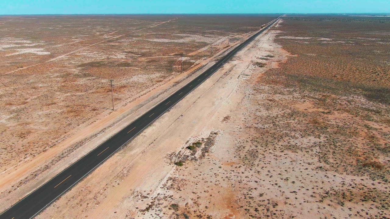 Aerial view of a straight paved road crossing sandy desert scrub.