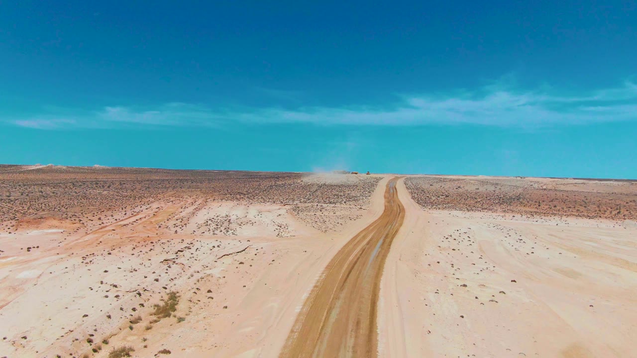 Aerial frame in Guerrero Negro, Baja California Sur showing a sandy dirt road leading toward a distant dust plume across sparse desert, with no visible people.