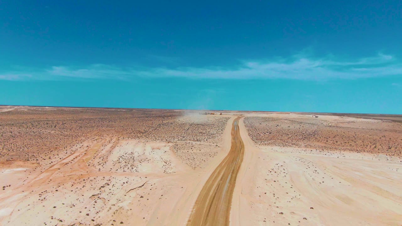 Aerial footage over Guerrero Negro, Baja California Sur shows the road narrowing into the horizon while a light dust trail hangs near the far section, with no visible people.