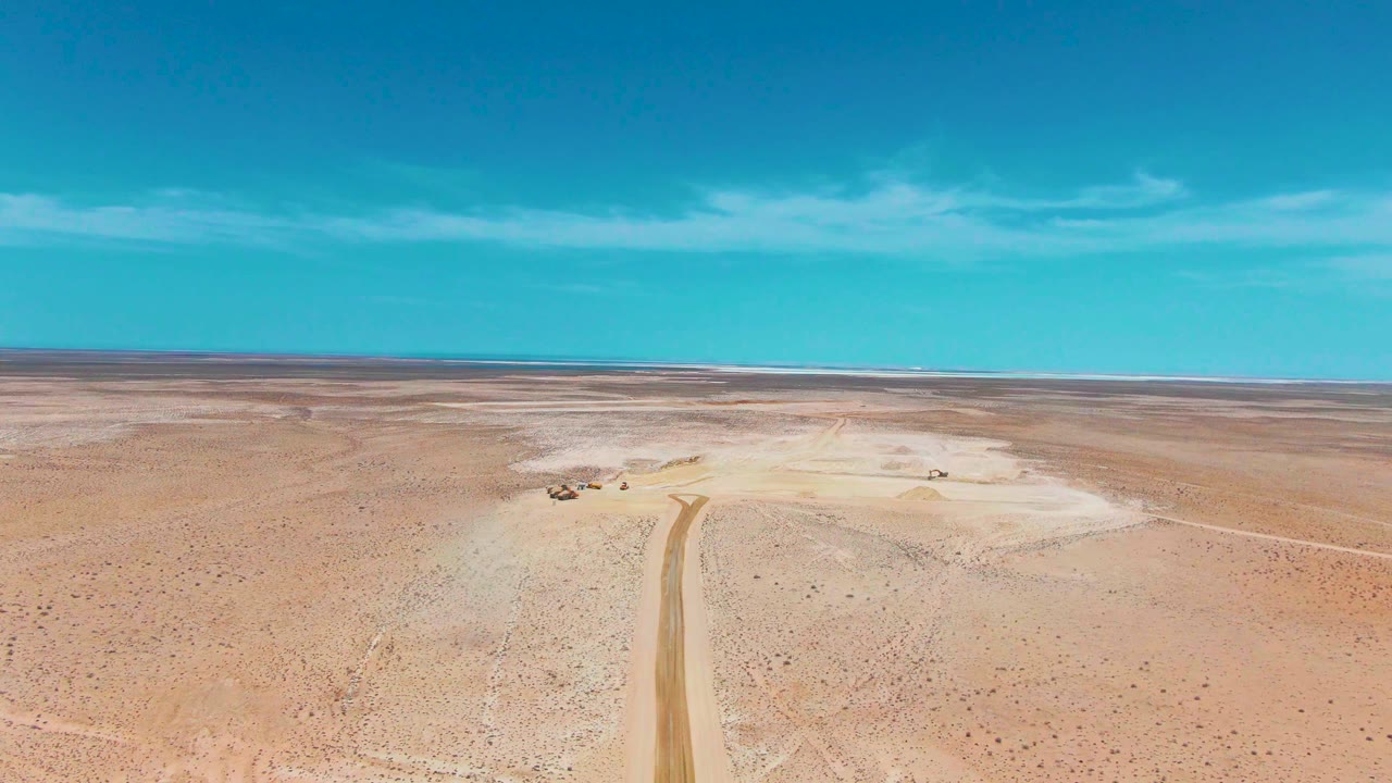 Drone-style aerial frame from Guerrero Negro, Baja California Sur showing a small vehicle beside a light dirt road, open sandy ground, distant horizon, and no visible people.