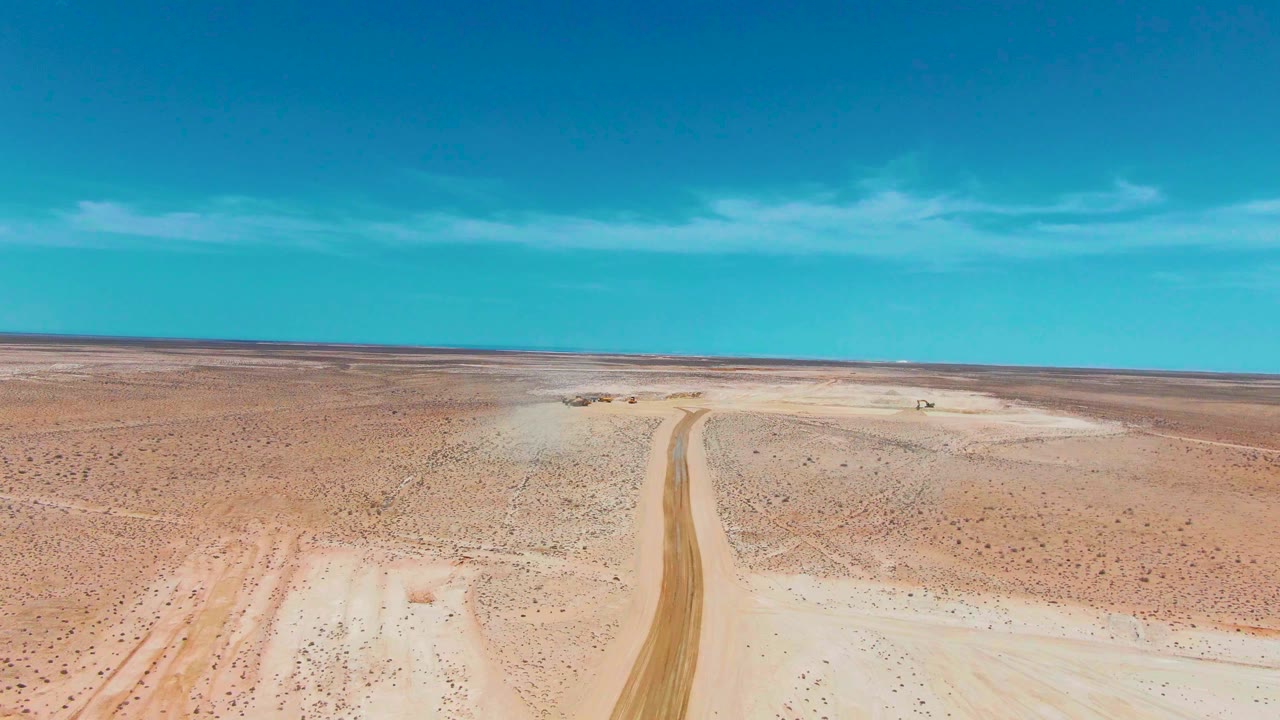 Dirt track and small vehicle in a broad desert aerial view.