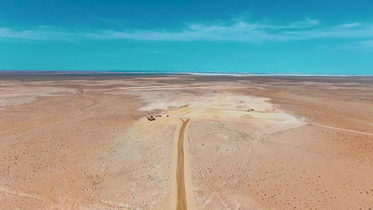 Wide aerial desert with dirt road and small vehicles near pale ground.