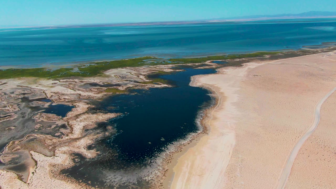 Aerial view of dark lagoon water beside pale sand and blue ocean.