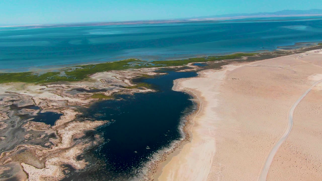 Aerial view of dark lagoon beside pale sand and turquoise ocean