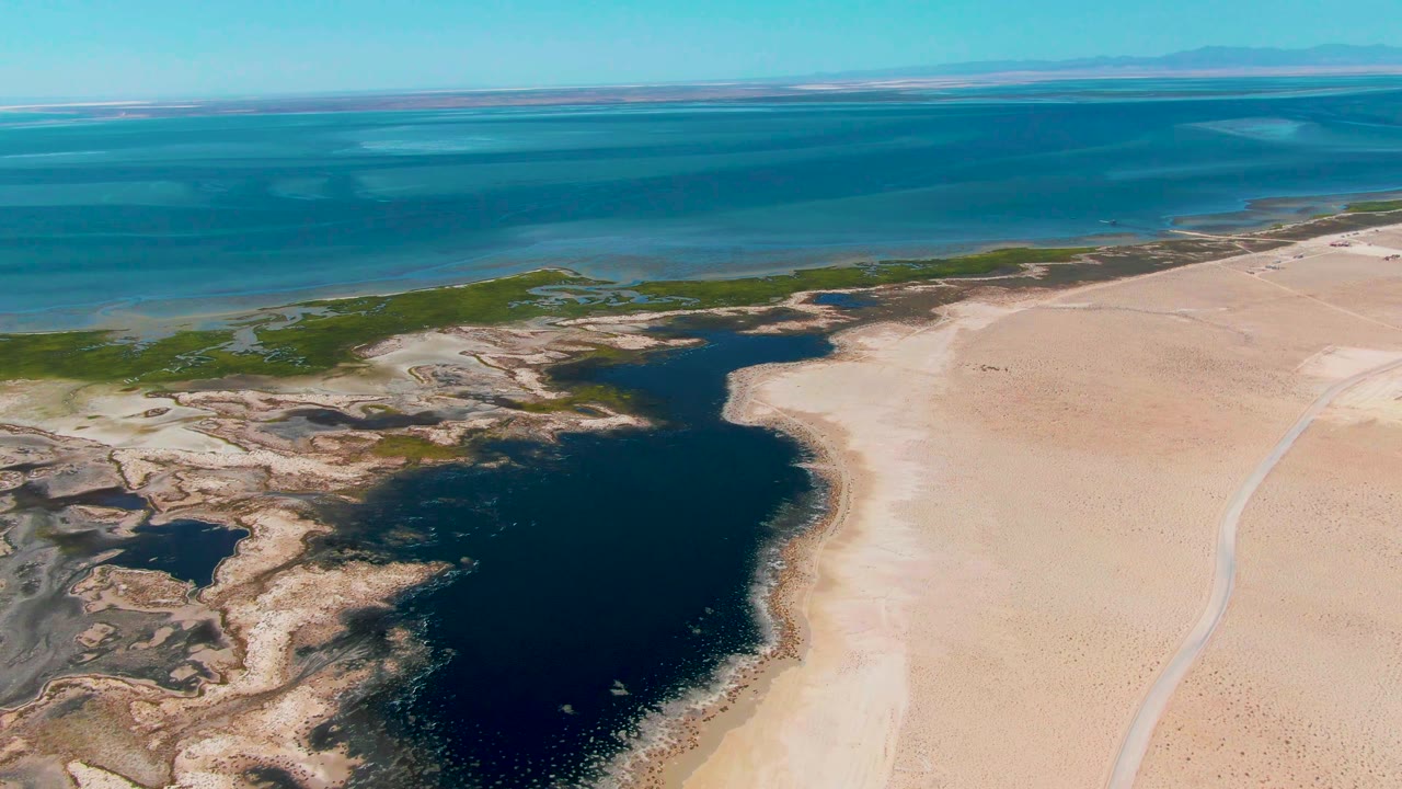 Aerial view of a dark lagoon beside pale sand and blue ocean.