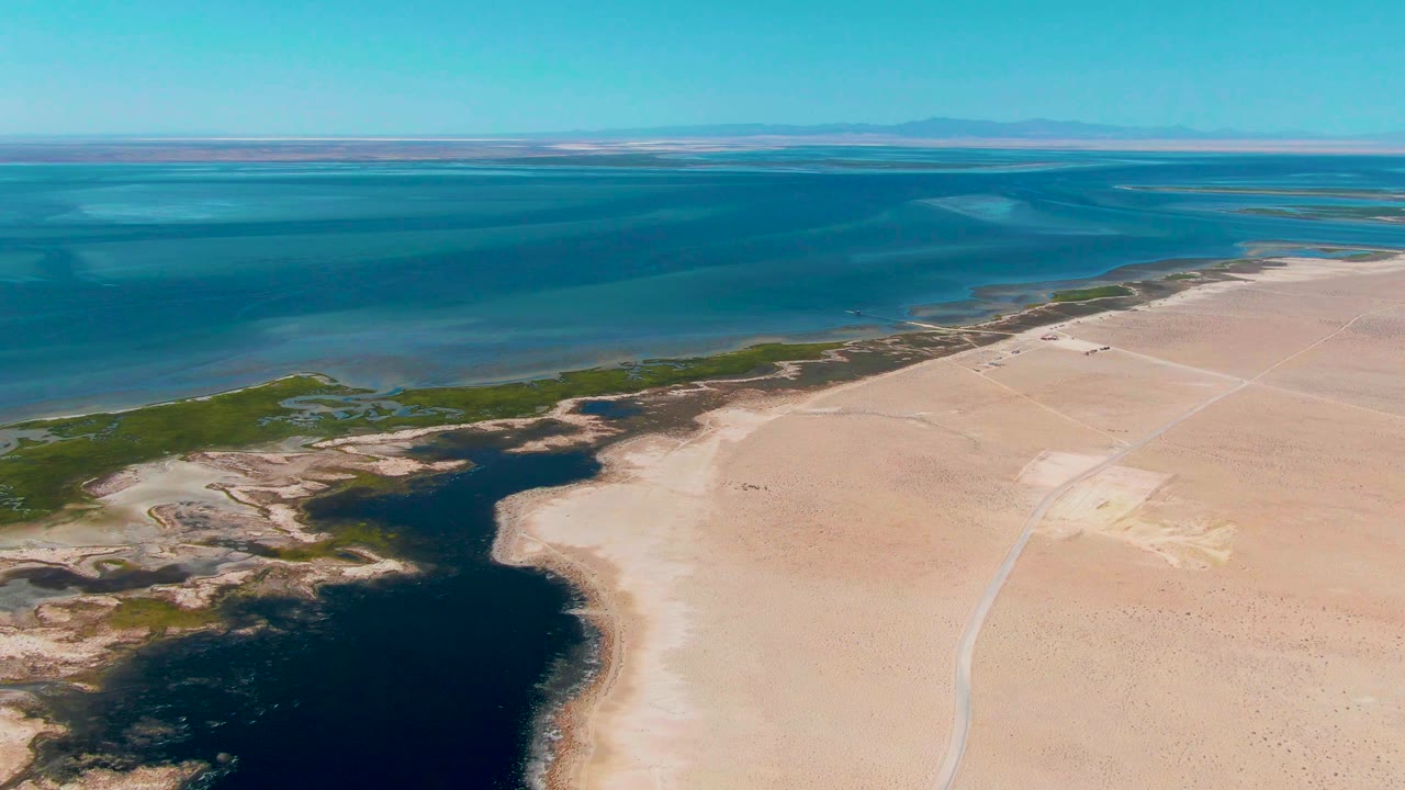 Aerial shoreline with dark lagoon foreground, green marsh, sand, and blue water.