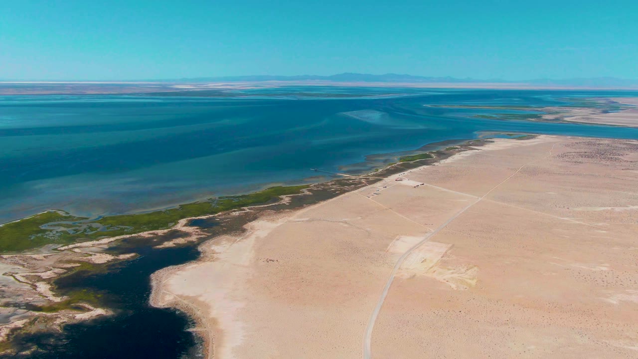 Aerial view of blue water beside sandy shoreline and sparse green vegetation.