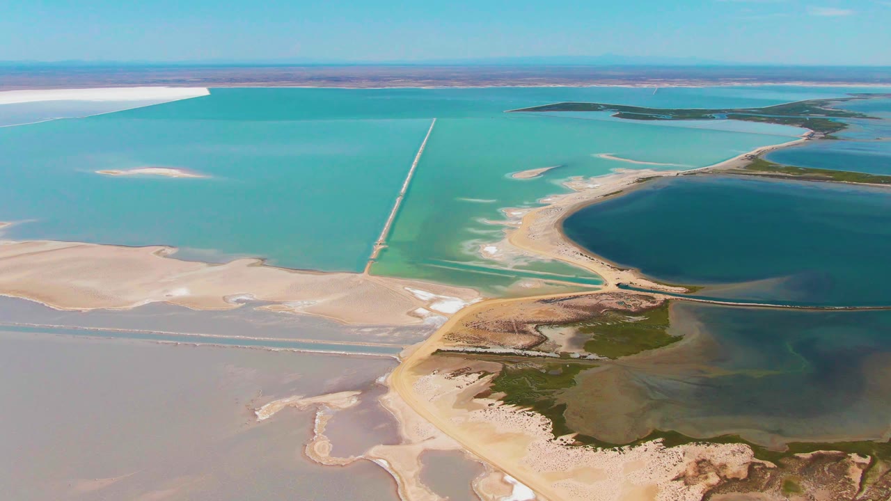 Aerial view of turquoise salt ponds, white flats, dry land, and a long causeway.