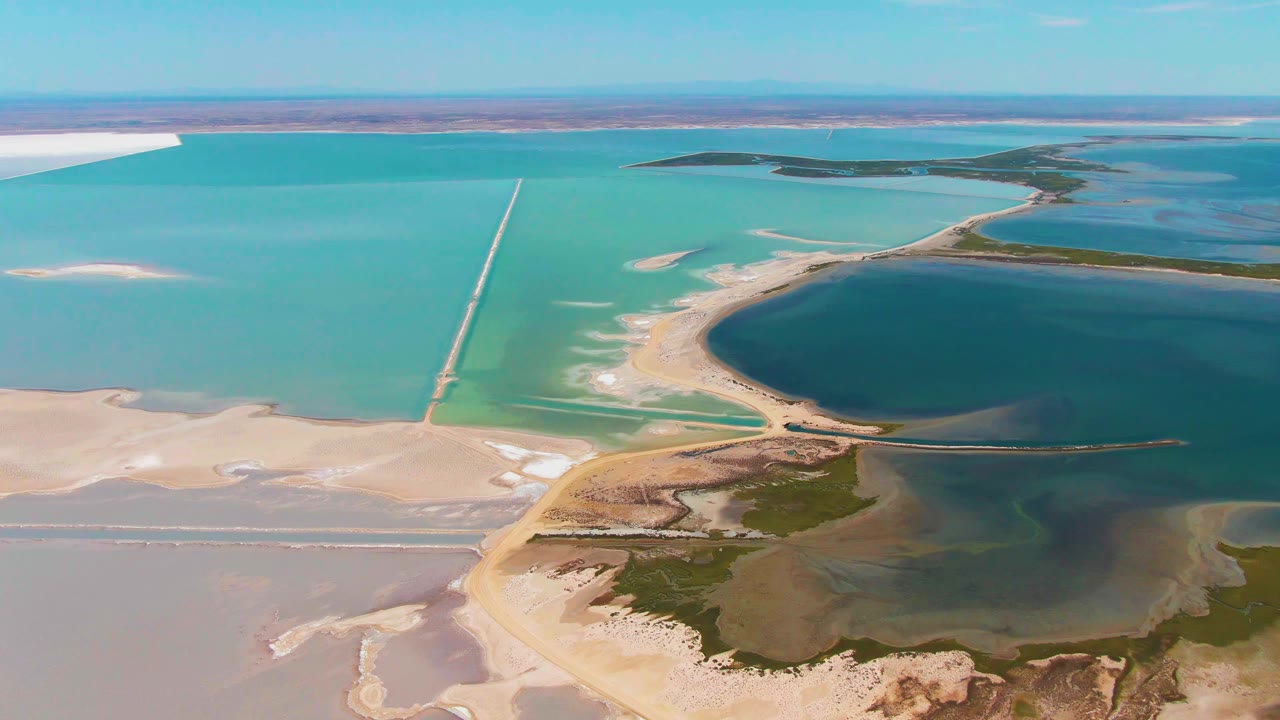 Guerrero Negro aerial frame with a long straight causeway cutting through turquoise shallows, a darker water basin on the right, white salt flats on the left, and no visible people.