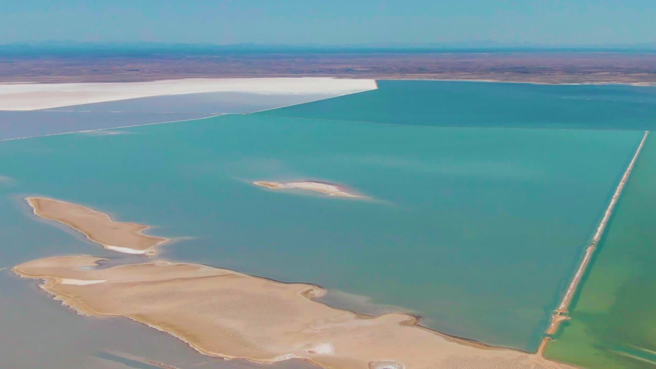 Aerial view of turquoise salt lake with beige sandbars and a narrow causeway at right.