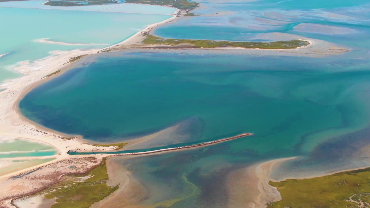 Aerial view of turquoise lagoon water, sandy shores, and a narrow breakwater