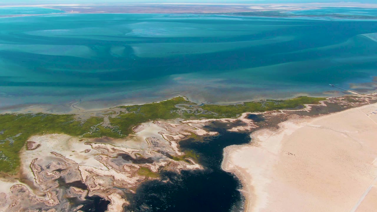 Drone-like aerial view of ocean, marsh, and beach sand.