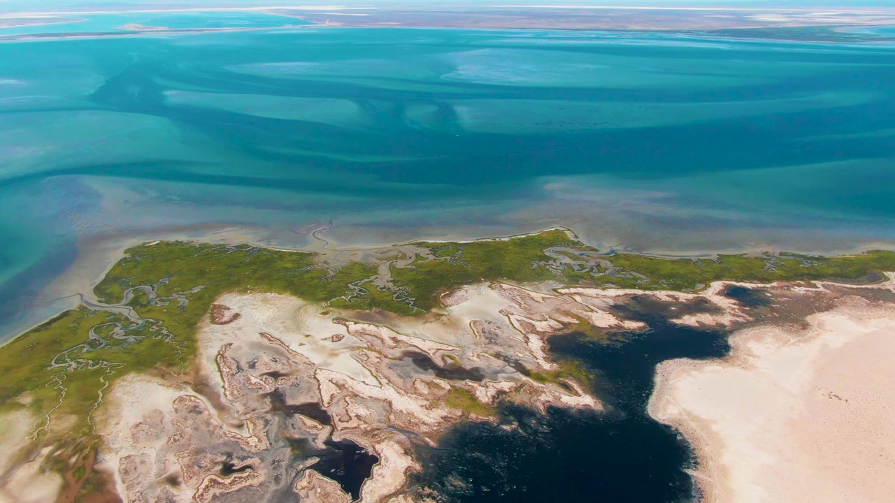Aerial view of turquoise water beside sandy and rocky shoreline
