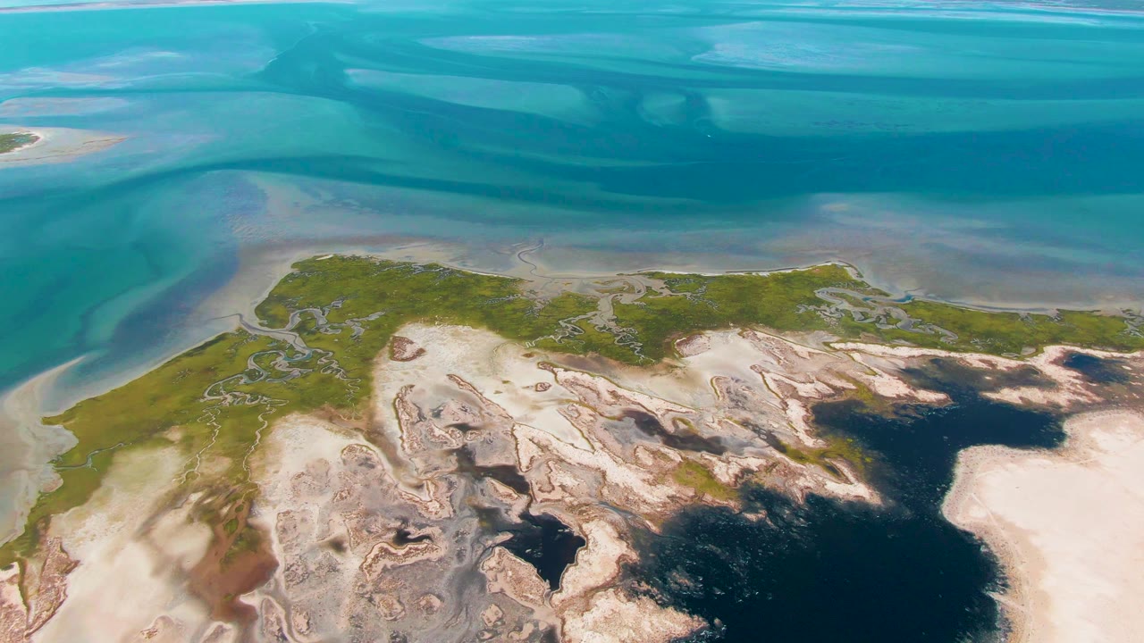 Aerial view of turquoise water, sandbars, and a green coastal landmass.