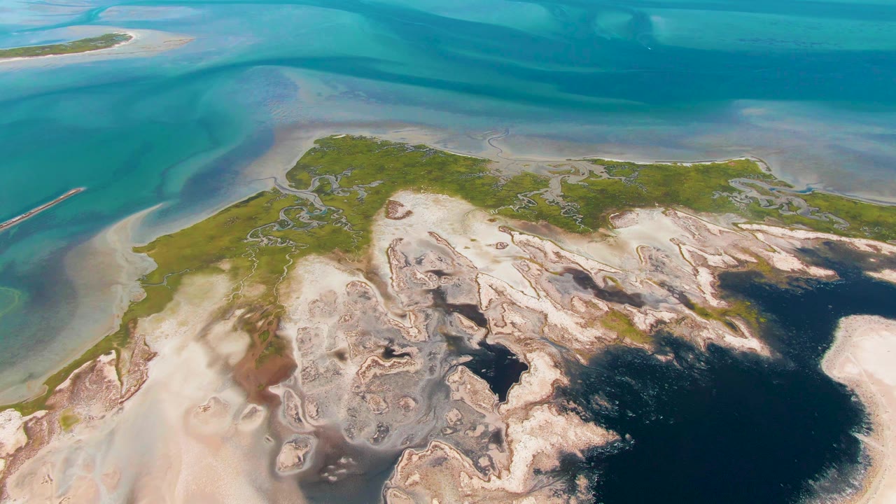 Third aerial frame from Guerrero Negro with turquoise water at the top, a green marsh band along the shore, pale tidal flats below it, dark wet pools to the right, and no visible people.