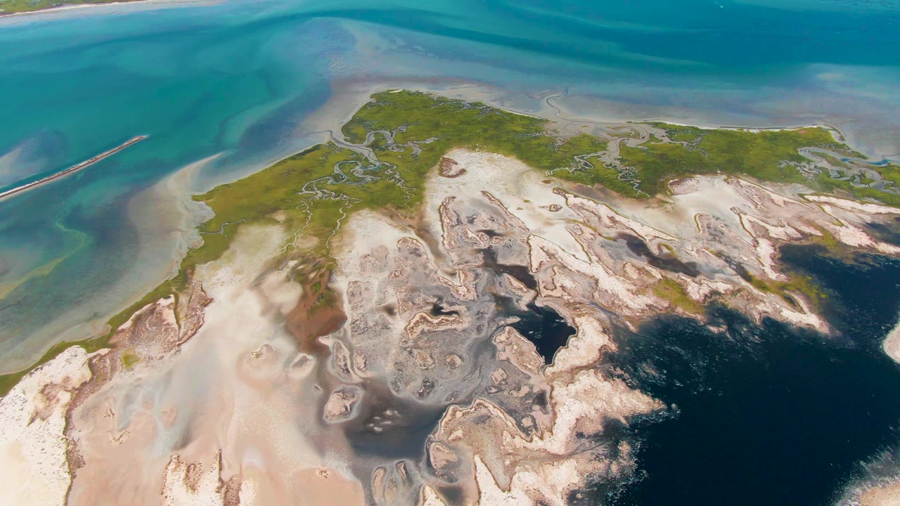 Overhead view of Guerrero Negro shoreline with pale sand flats, green vegetation, turquoise shallows, dark blue water, and no visible people at the start of the clip.