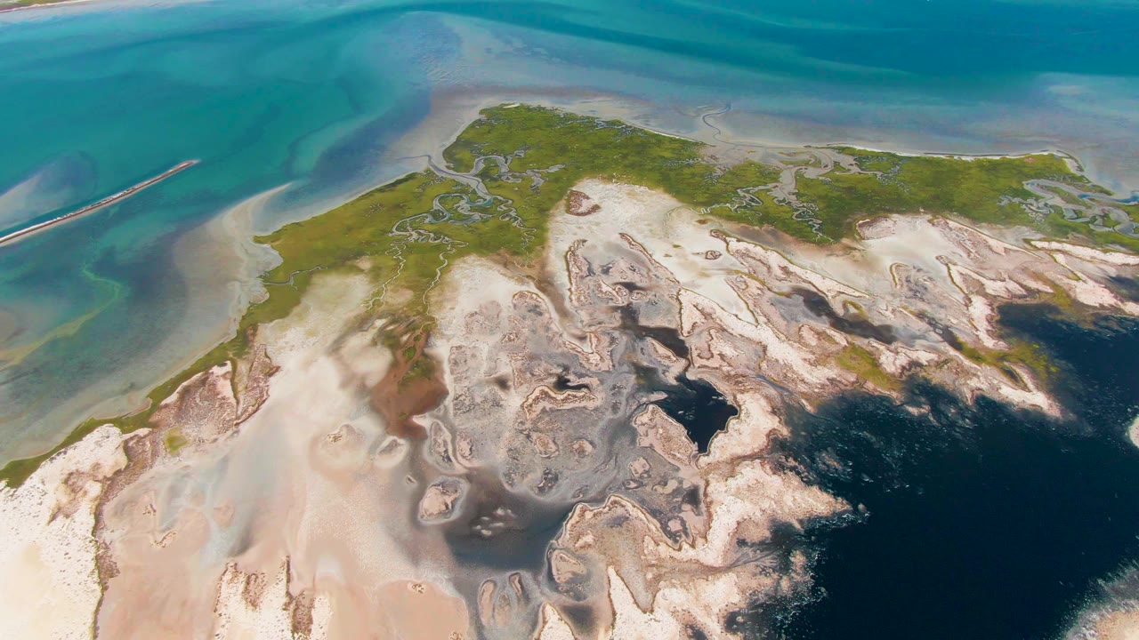 Aerial shoreline with green land, pale sand, turquoise water, and dark shadow across the lower right.