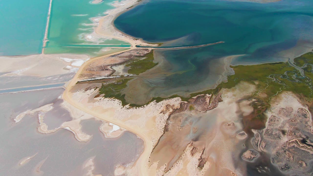 One second into the Guerrero Negro clip, the aerial view holds on the sandy spit, dark blue lagoon water above it, pale wet flats below it, and no visible people.