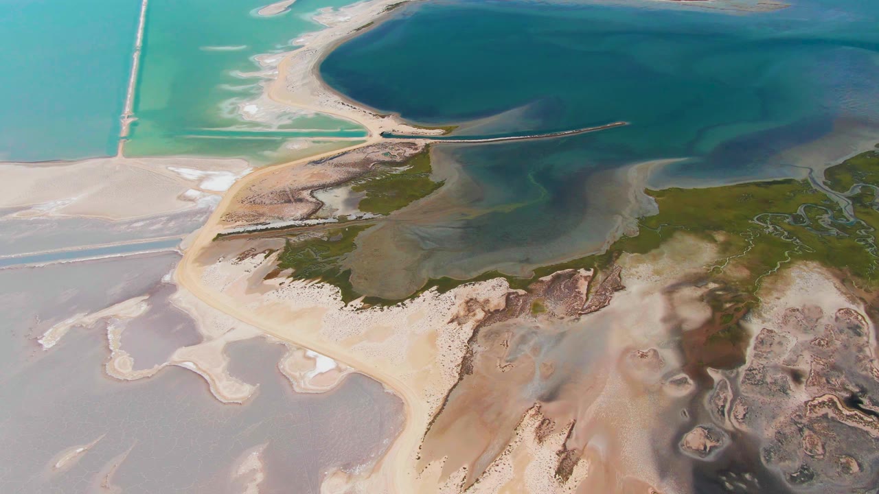 At 0:02, the Guerrero Negro aerial frame shows a curved pale sandbar between blue-green water, darker lagoon water, mottled wetland, and exposed sand with no visible people.