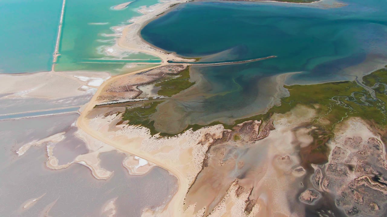 At 0:03, the Guerrero Negro drone view continues across pale tidal flats, a central sandbar, green-brown marsh texture, darker water, and no visible people.