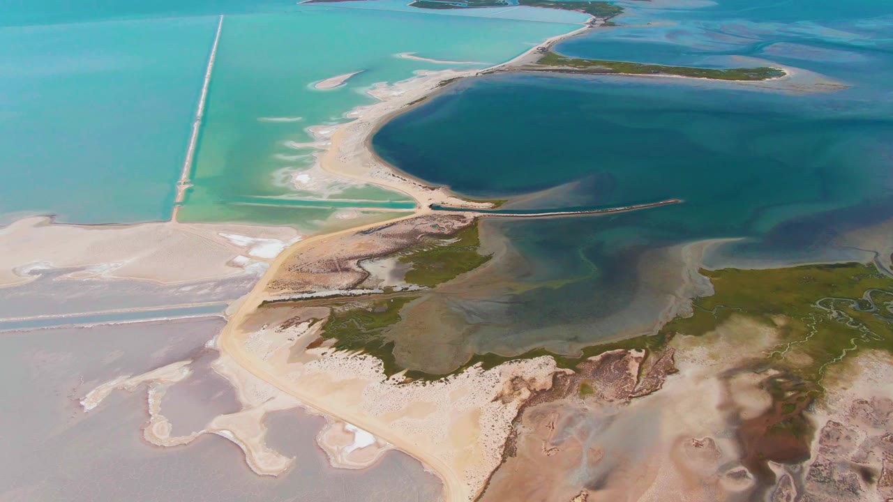 One second into the clip, the aerial view over Guerrero Negro shows the straight causeway more centered against turquoise water, pale sand, salt flats, green shoreline, and no visible people.