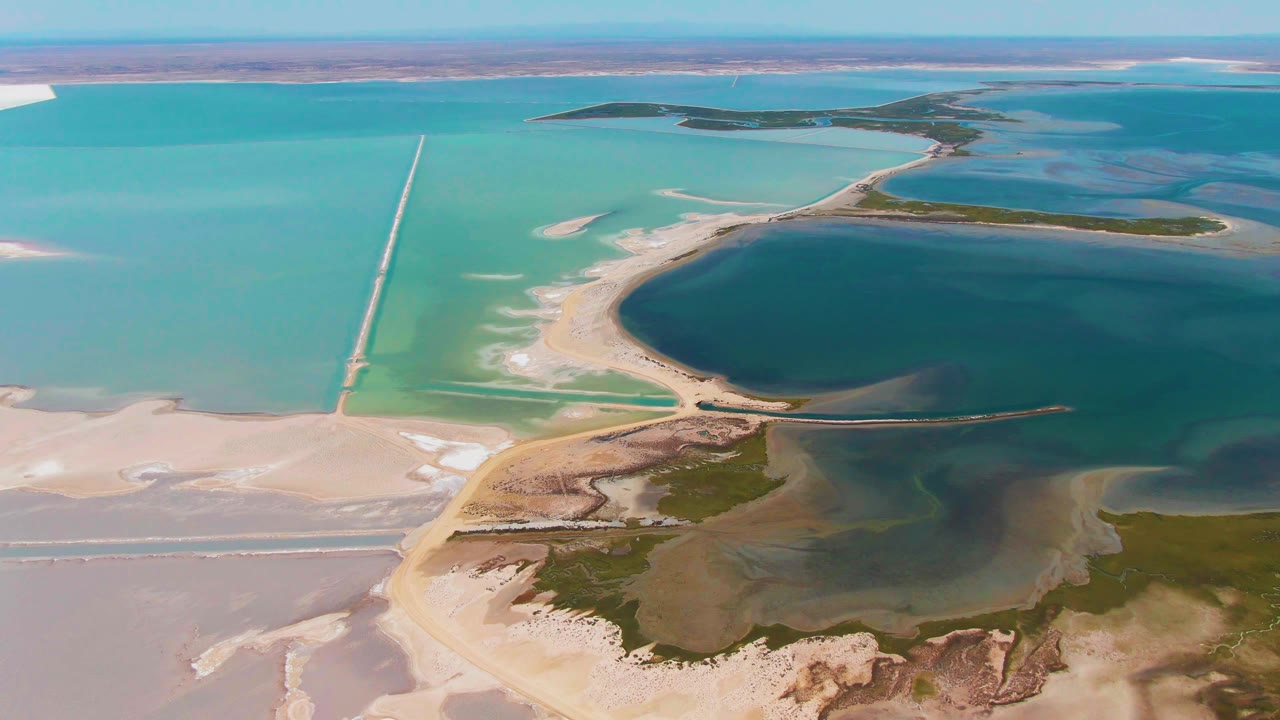 Second frame over Guerrero Negro shows the straight causeway left of center, bright turquoise water around sandbars, darker lake water on the right, exposed salt flats below, and no visible people.