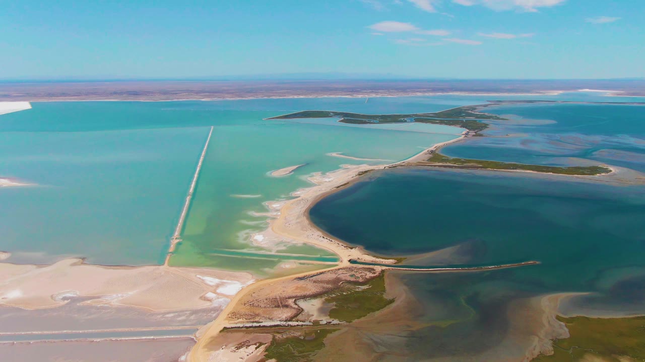 One second into the clip, the Guerrero Negro aerial view centers the causeway more clearly against turquoise water, with a dark blue basin, pale shoreline sediment, distant islands, and no visible people.