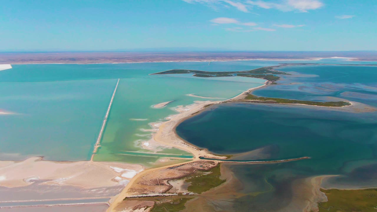 Midway through the clip, the aerial view over Guerrero Negro shows more open turquoise water to the left of the causeway, a dark basin to the right, a narrow road edge, and no visible people.