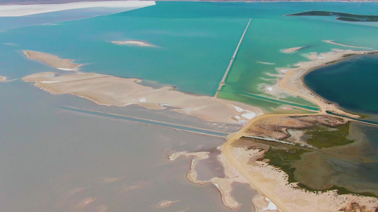 Aerial view of turquoise water, sandbars, shoreline, and a long straight structure.