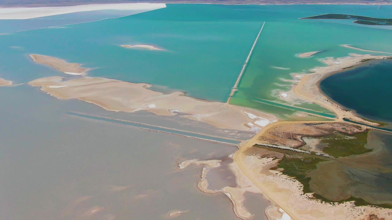 Aerial frame from Guerrero Negro, Baja California Sur, with the sandbar cluster more centered, the long straight structure running upward through turquoise water, and no visible people.