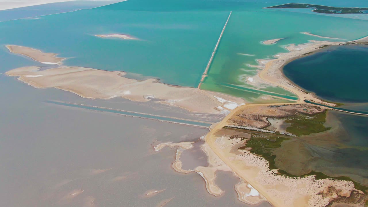 Aerial wetland frame with pale sand, turquoise water, and cloud shadow near the top.