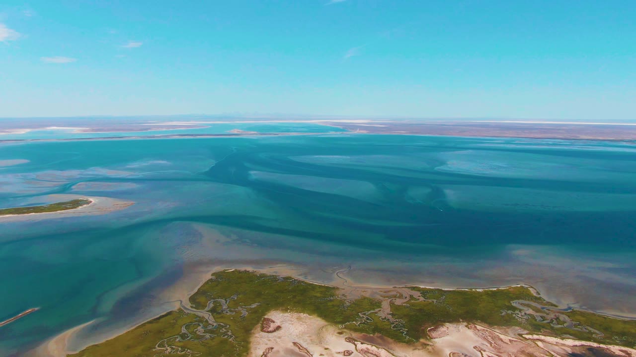 Guerrero Negro aerial view with turquoise and darker blue water bands across the middle, sandy flats near shore, green patches in the foreground, and no visible people.