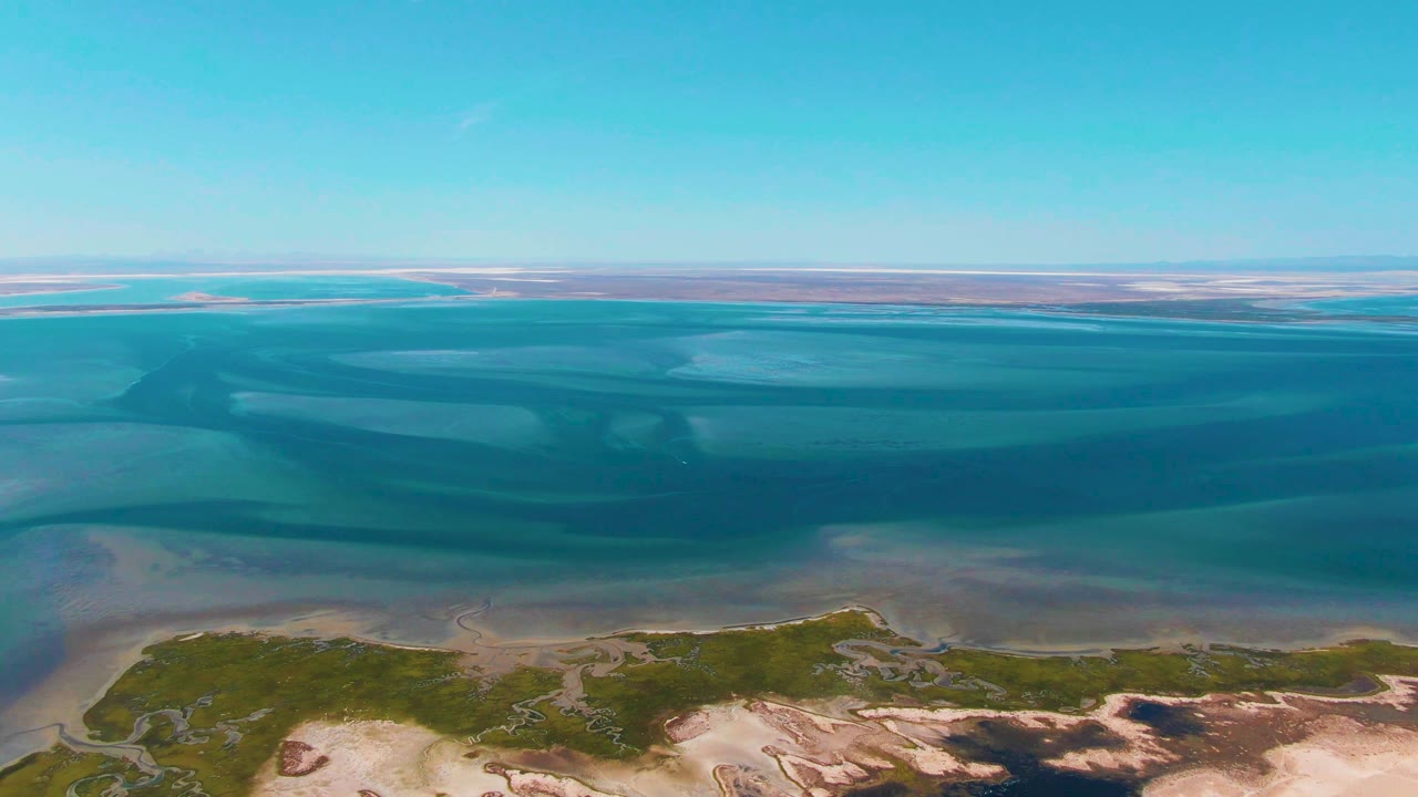 Aerial shoreline with dark blue water bands and pale sand flats.