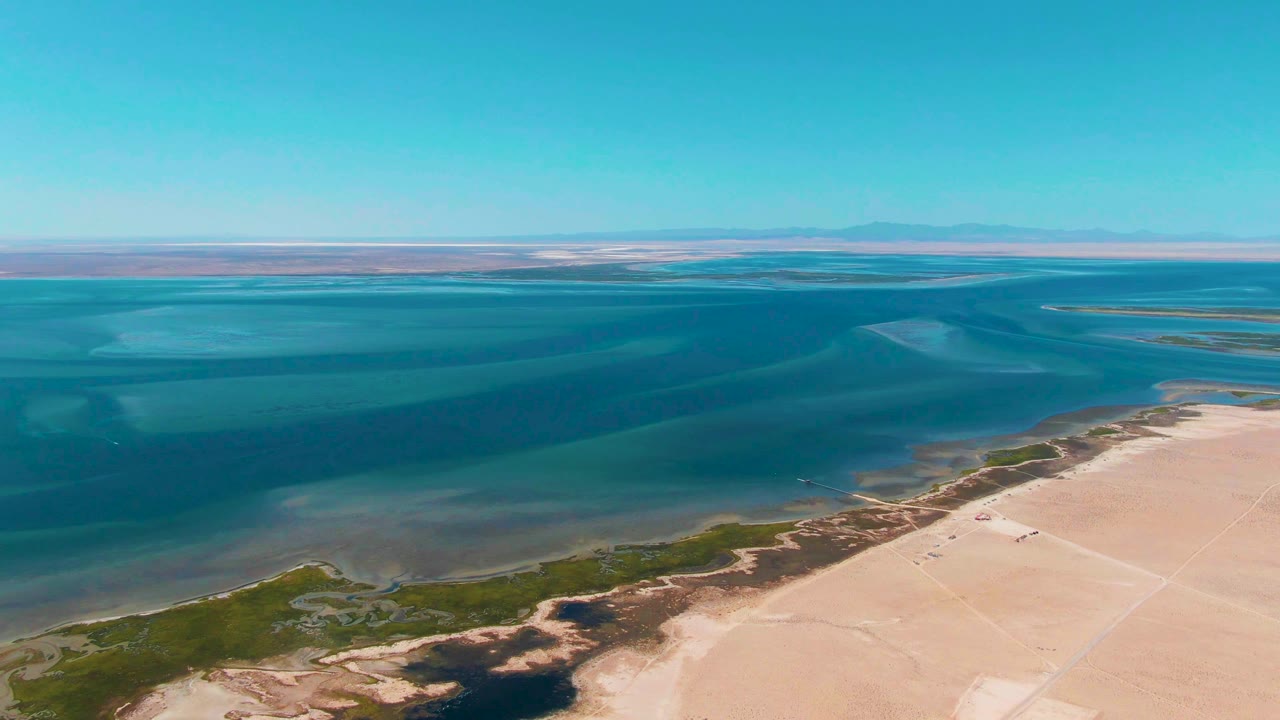 Wide aerial coast with shallow water color bands and pale sand flats.