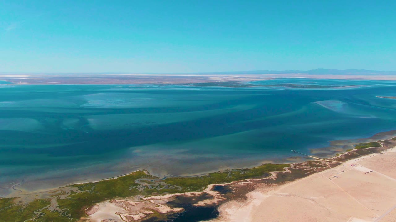 Coastal water, pale sand, and low green vegetation viewed from above.