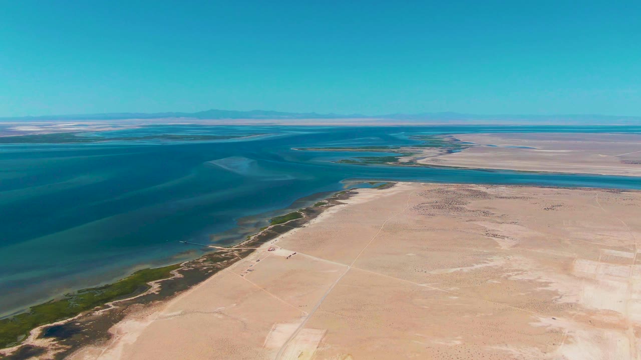 Wide aerial coastline with blue water and dry flat land.