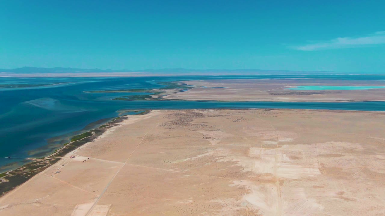 Aerial view of blue lagoon water beside a sandy plain under clear sky.
